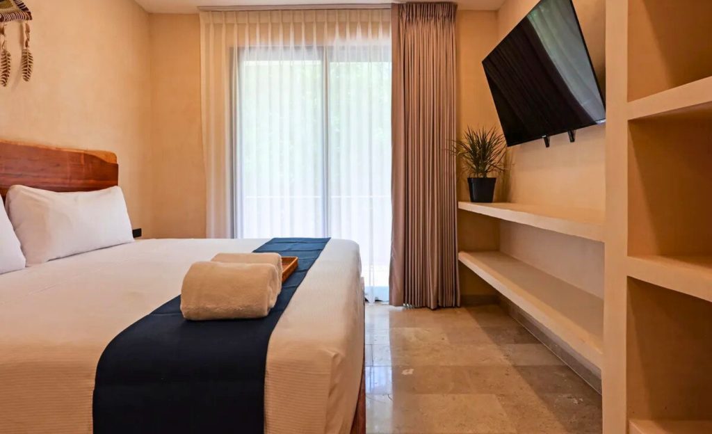 Elegant hotel room interior featuring a comfortable bed, stylish furnishings, and natural light streaming in from large windows.