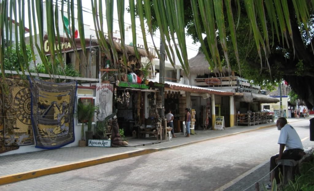 Bustling street in Tulum town with colorful shops, local restaurants, and tropical greenery lining the sidewalks.