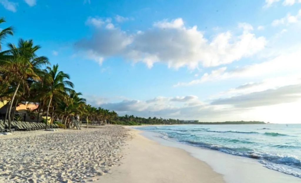 Beach with a few lounge chairs and plenty of sand on a sunny day.