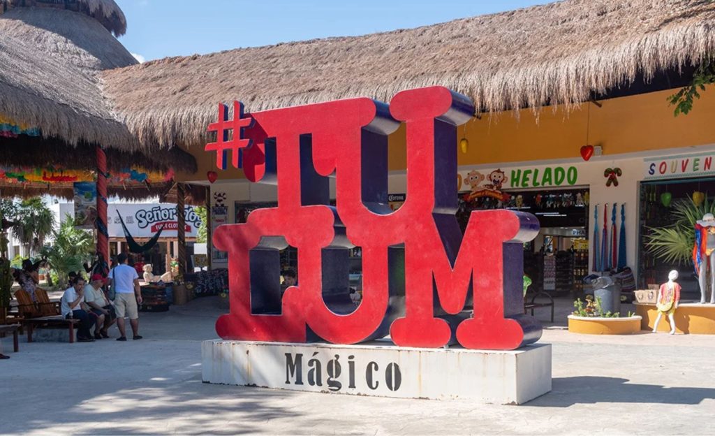 Central plaza in Tulum with people walking and a red Tulum sign in the foreground.