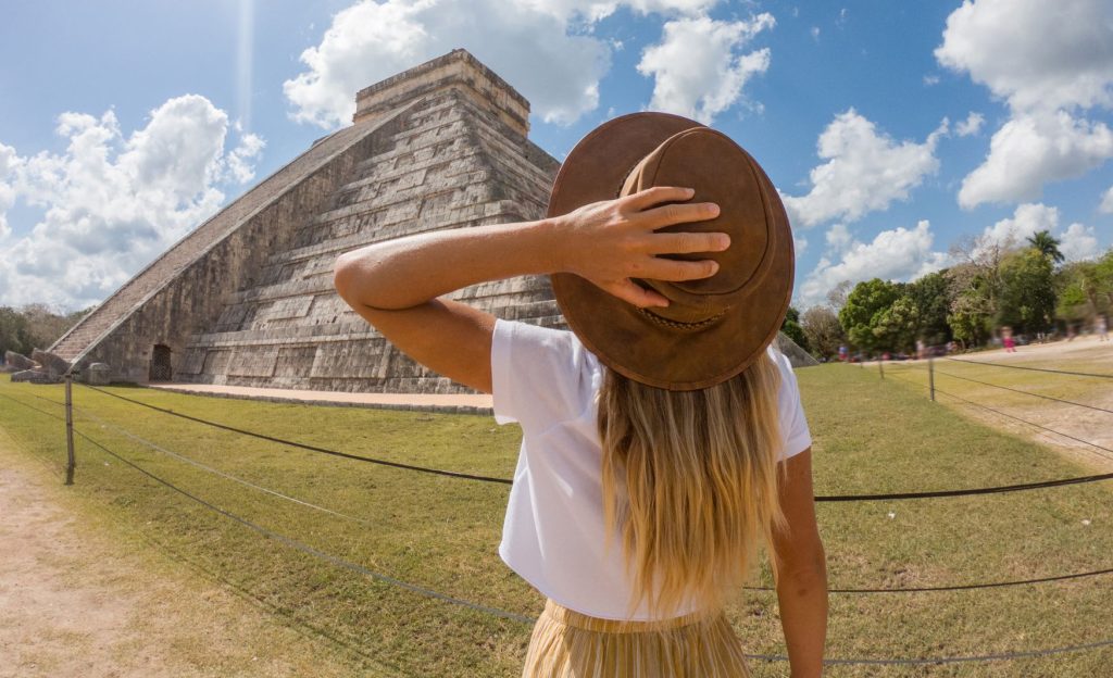 A young woman gazing at an ancient pyramid in Quintana Roo, Mexico, surrounded by lush greenery and a sense of history.