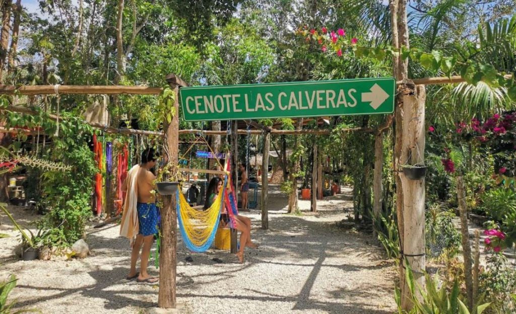 Entrada del Cenote Calavera Tulum con gente sentada en hamacas coloridas y mucha vegetación