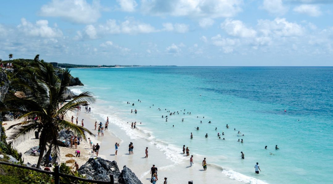 Tulum beach with crystal-clear waters in multiple shades of blue, as swimmers enjoy the warm Caribbean waves.