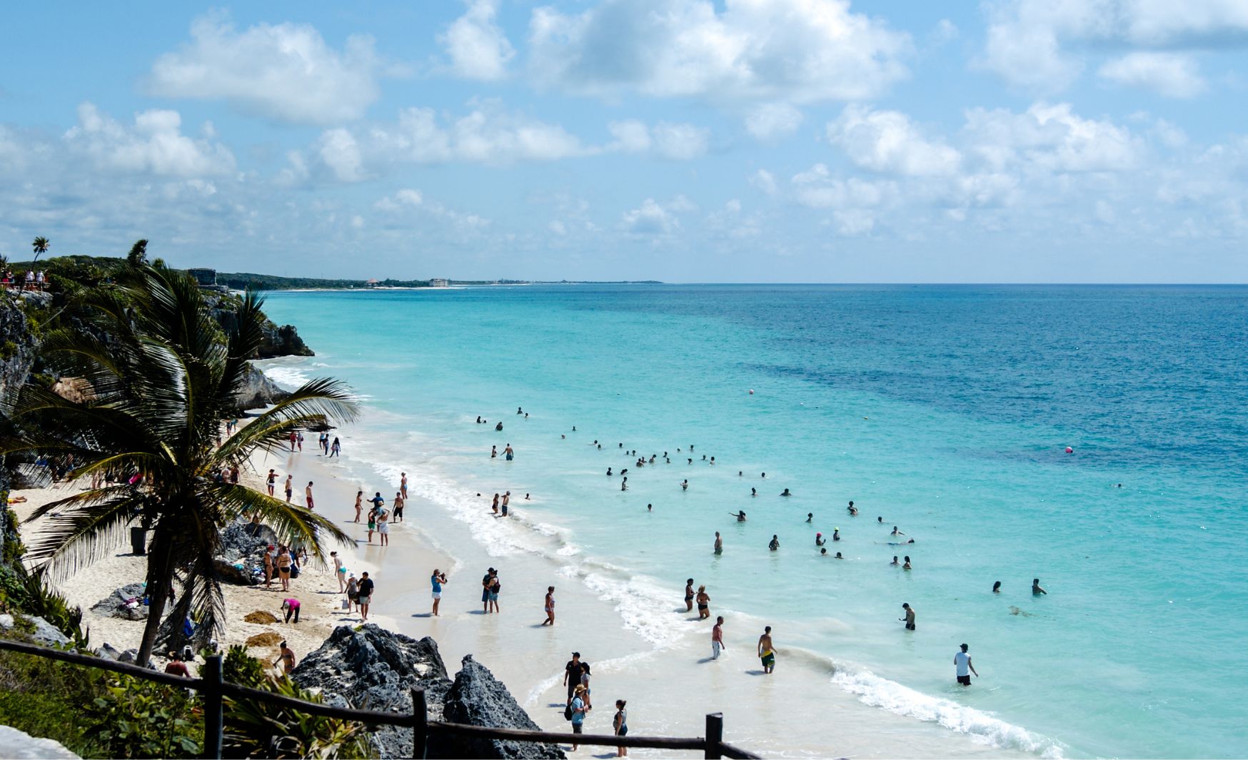 Tulum beach with crystal-clear waters in multiple shades of blue, as swimmers enjoy the warm Caribbean waves.