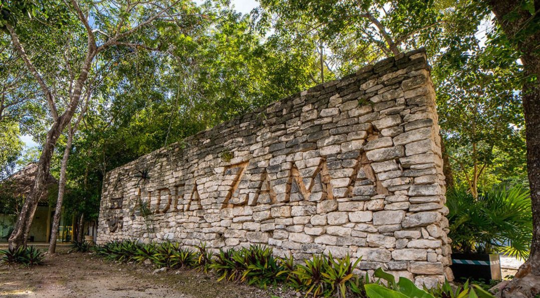 Stone sign marking the entrance to Aldea Zama, surrounded by lush greenery and tropical vegetation in Tulum.