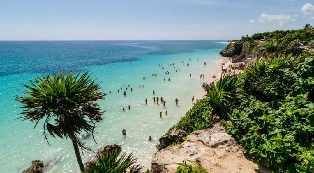A beautiful beach in Tulum with crystal-clear water and people swimming, showcasing the pristine environment. Is Tulum expensive for beachgoers?