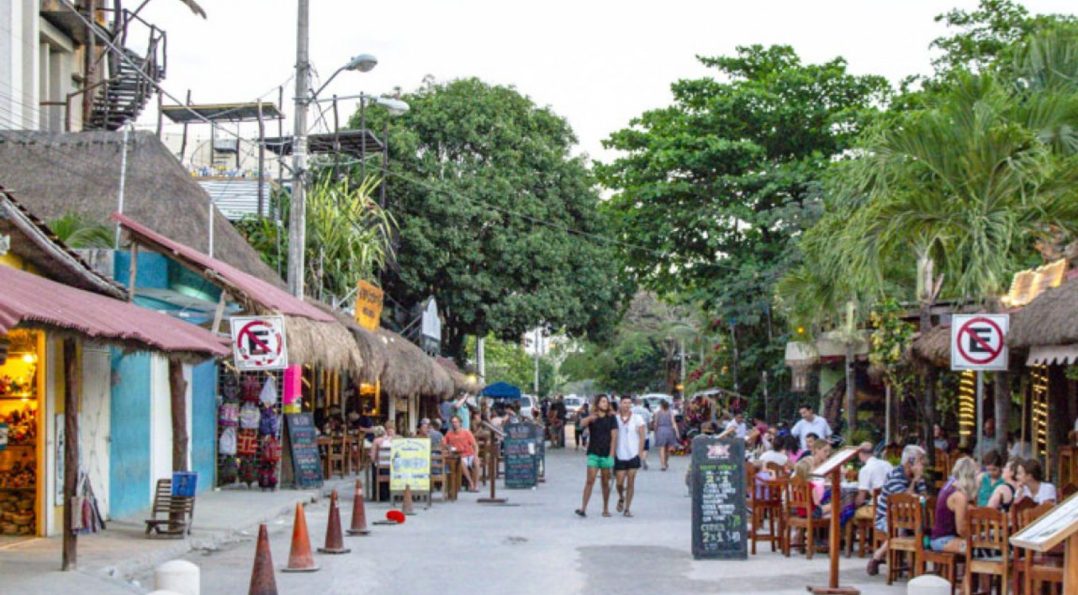 A bustling street in downtown Tulum with tourists walking among vibrant shops and restaurants.