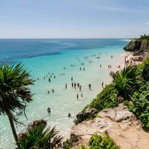 A beautiful beach in Tulum with crystal-clear water and people swimming, showcasing the pristine environment. Is Tulum expensive for beachgoers?