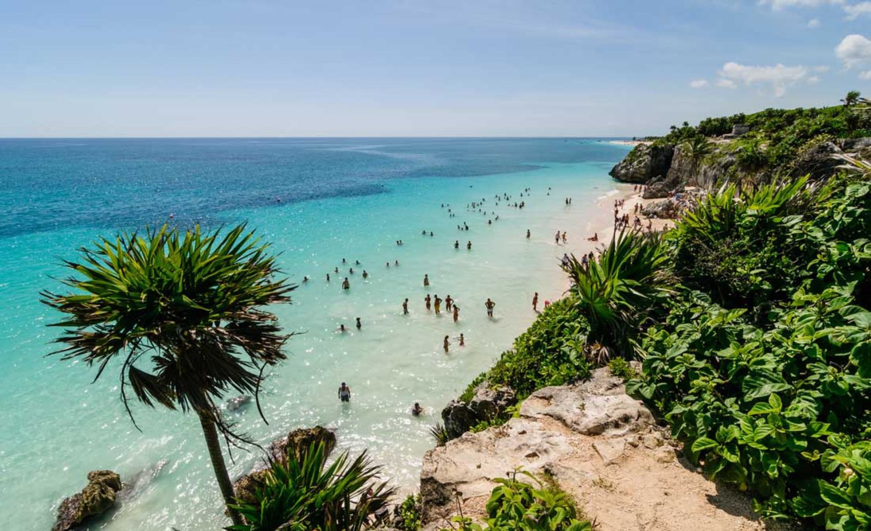 A beautiful beach in Tulum with crystal-clear water and people swimming, showcasing the pristine environment. Is Tulum expensive for beachgoers?